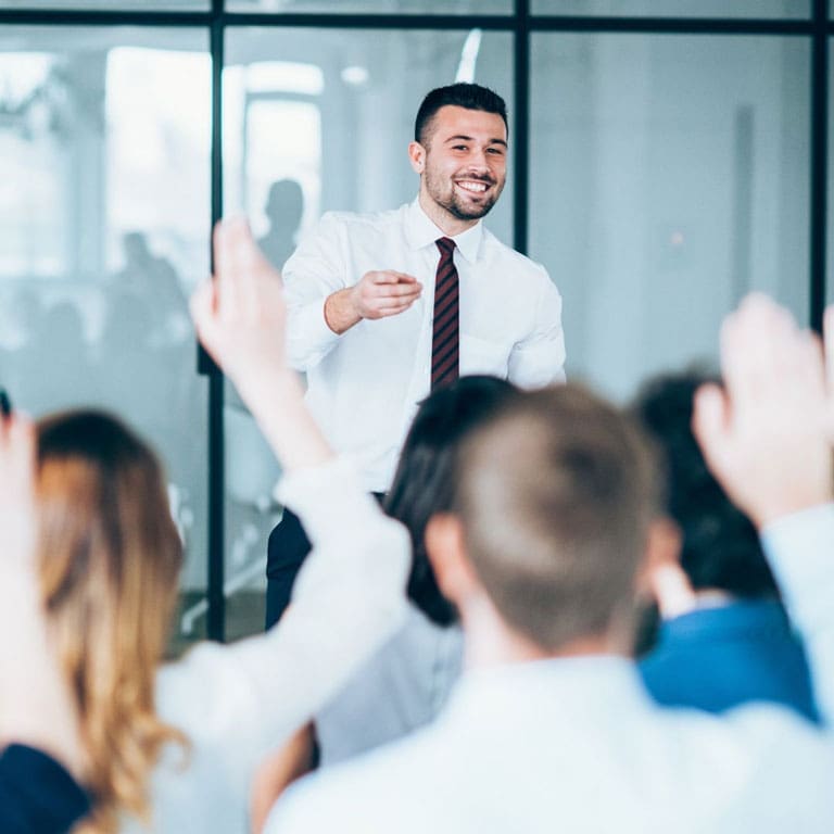 Insegnante parla ad un gruppo di persone con la mano alzata che seguono i Corsi Executive per business angel di Impact hub Milano